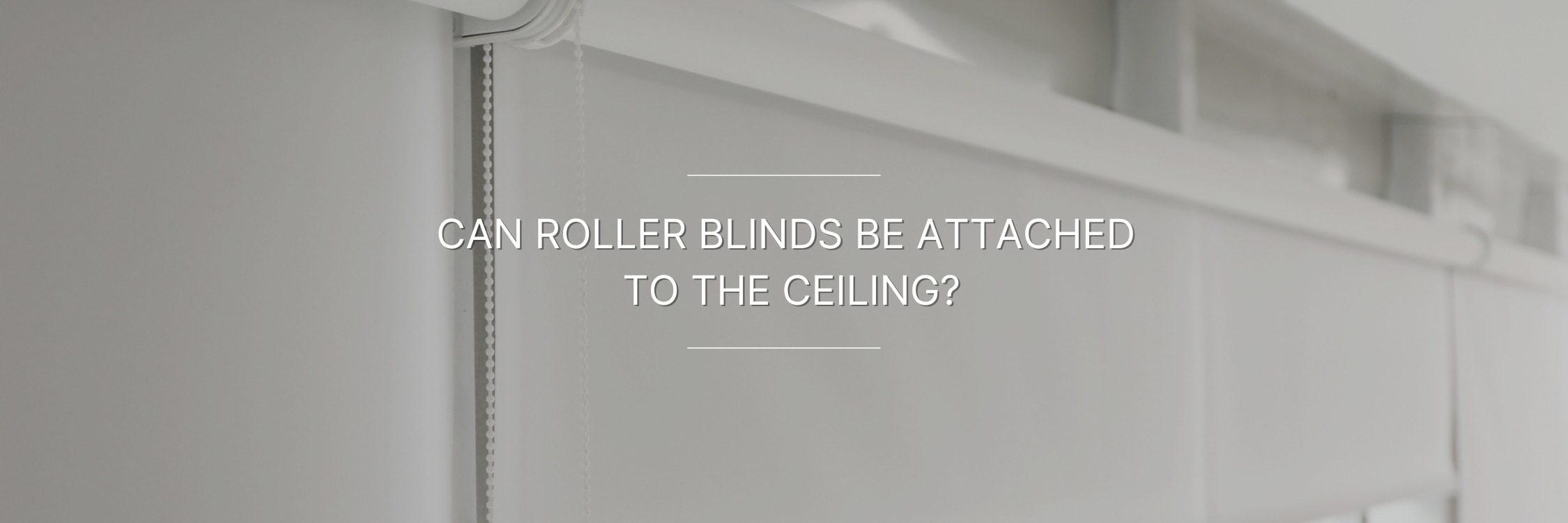 A close-up image of a roller blind mounted to the ceiling. The blinds are closed and the fabric is a light gray color.