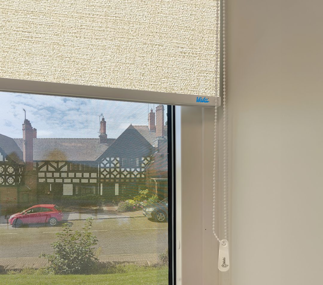 closeup view of a window with a light beige roller blind, showing a historic building and parked cars outside.