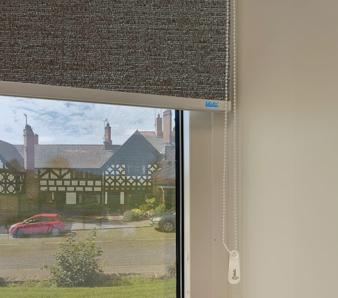 closeup view of a window with a dark grey roller blind, showing a historic building and parked cars outside.
