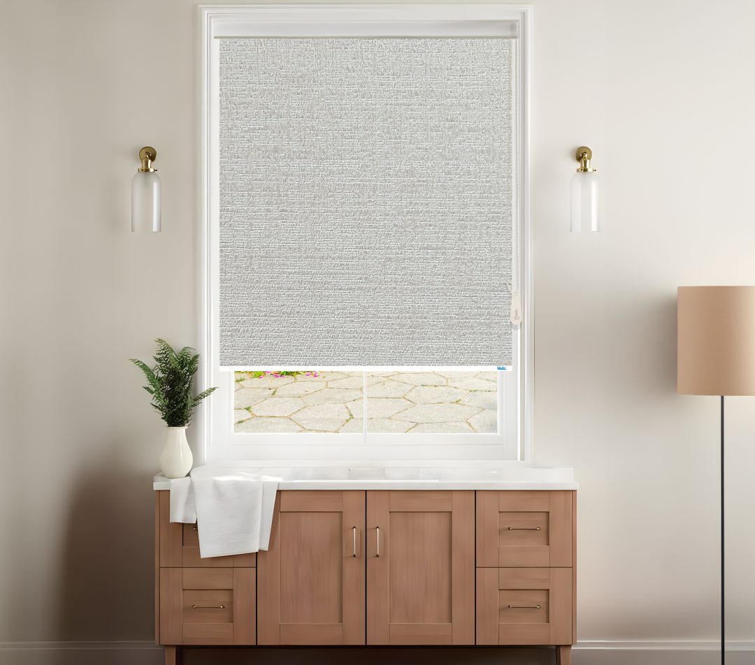 A stylish room features a grey blackout venice roller blinds covering a window with a view of a stone patio, complemented by modern decor.