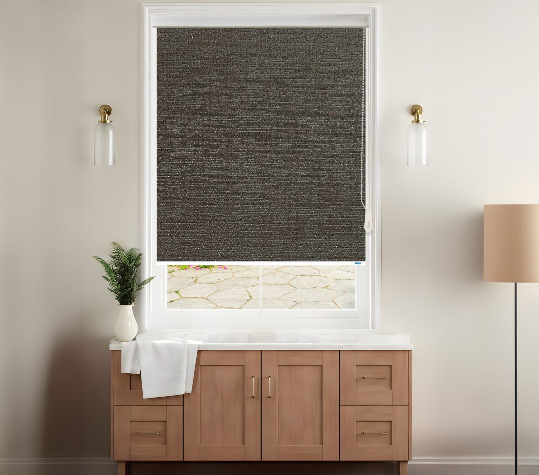 A stylish room features a dark woven blackout venice roller blinds covering a window with a view of a stone patio, complemented by modern decor.