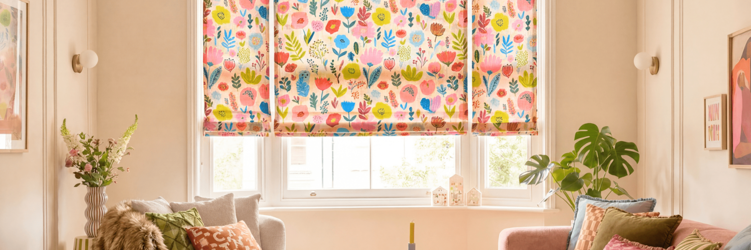 Cozy living room with large windows covered by colorful floral Roman shades, neutral walls, and comfortable sofas with patterned pillows.