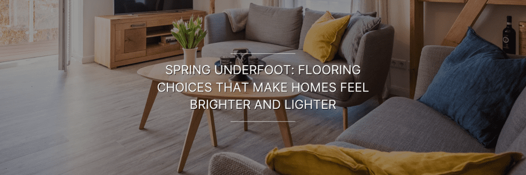 Cozy living room with light wood flooring, gray sofas with colorful cushions, a round wooden coffee table, and a TV stand with flowers.