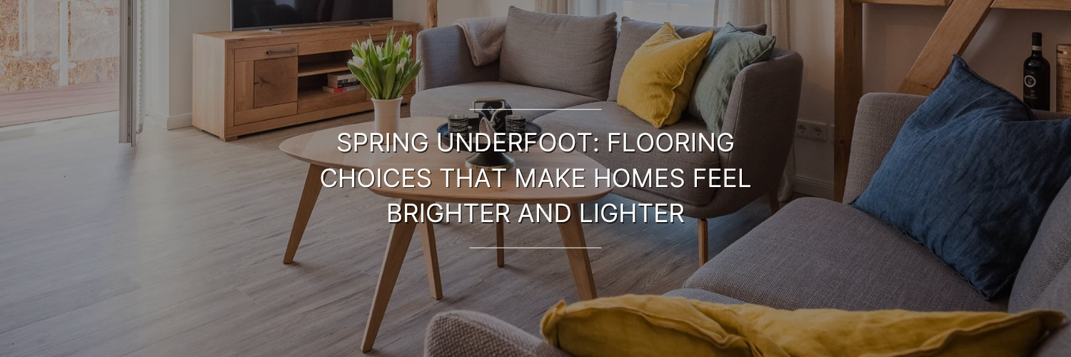 Cozy living room with light wood flooring, gray sofas with colorful cushions, a round wooden coffee table, and a TV stand with flowers.