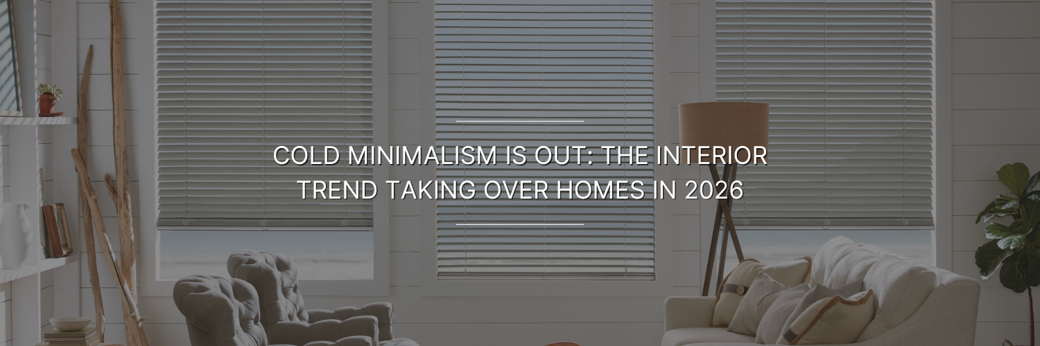 Modern living room with neutral tones features comfortable couches, decorative ladder, floor lamp, and plants. Large windows with blinds filter light. Text overlay reads: "Cold Minimalism is Out: The Interior Trend Taking Over Homes in 2026."