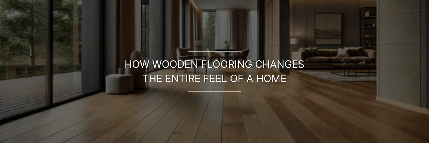 Wooden-floored living room with large windows overlooking a forest. Cozy furniture and soft lighting create a warm, inviting atmosphere. Text overlay reads: "How wooden flooring changes the entire feel of a home.